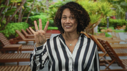 Hispanic woman hand ok sign gesture while smiling in green park outdoors under bright sunlight;...