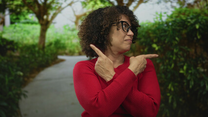 Woman in red sweater wearing glasses pointing finger in lush green forest path; confidence...