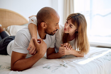Happy interracial couple laying in bed, embracing each other with affection, celebrating their loving and intimate relationship