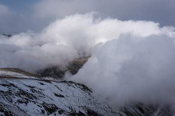 Dramatic high mountain landscape with snow, rocks and low clouds
