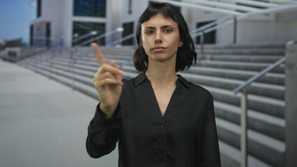 Young hispanic woman wearing black shirt with hand on chin by concrete building steps;...