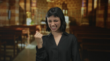 Young hispanic woman smiling and pointing finger at camera inside historic church building; joy...