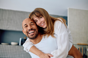 Cheerful diverse couple smiling broadly, woman getting a piggyback from man, embracing fun and...