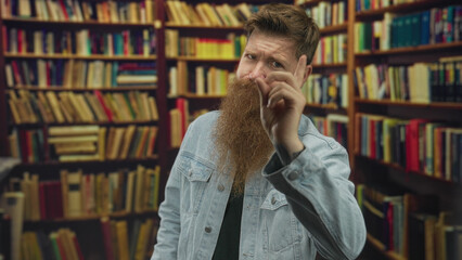 Man with long brown beard points finger at camera in library building with old wooden shelves;...