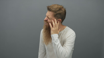 Man with full long beard grimaces and squints with mouth open while holding hand to ear showing...