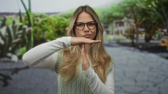 Woman wearing glasses makes timeout gesture with arms across chest in park; pause boundary reflection.