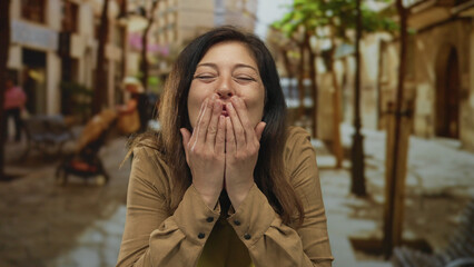 Woman wearing yellow shirt touches chest on a busy city street with blurred storefronts; gratitude sincerity.