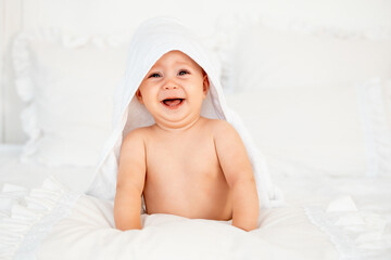 crying baby in a towel after a bath, a small happy baby on a bed in a white towel, space for text, baby hygiene and care