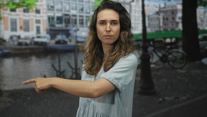 Young hispanic woman pointing finger with bare forearm toward canal on amsterdam street; calm...