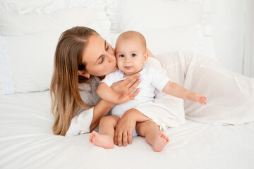 mother and baby hugging and kissing on the bed at home, maternal love and care, mother and child
