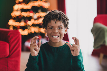 Joyful teen crossing fingers for holiday wishes in front of a festive Christmas tree