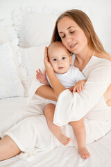 mother and baby hugging and kissing on the bed at home, maternal love and care, mother and child