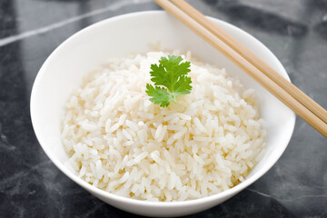 Cooked rice with coriander leaf in white bowl with chopsticks.