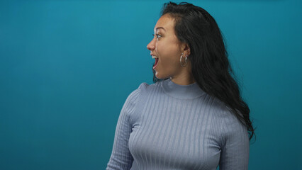 Woman face smiling with head turned, looking right in teal studio wearing light blue ribbed...