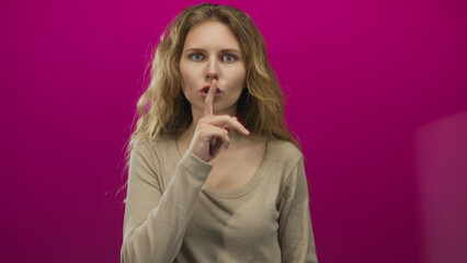 Fototapeta premium Woman finger shushing studio blonde young lips pink gesture silence poster evokes quiet mystery.