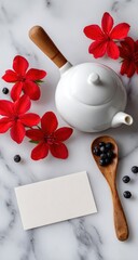 A white porcelain tea pot, red flowers, and a wooden spoon with berries sit atop a marble surface, with a blank business card in the center.