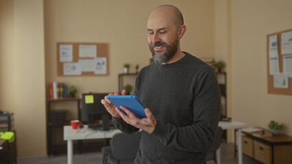 Man with beard using tablet in indoor office setting with plants and computer equipment surrounding him