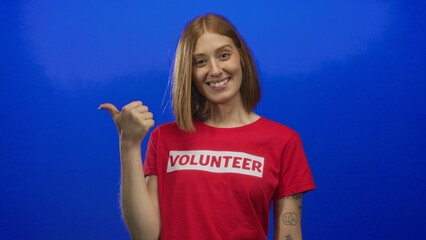 Young blonde volunteer points thumb to side in studio; approval encouragement support confidence.