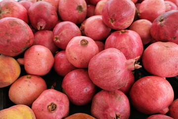 Fresh pomegranates and peaches arranged on a black plastic crate, likely at a market or fruit stand.