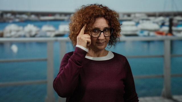 Woman standing by a seaside location with a marina backdrop, showcasing a thoughtful gesture.