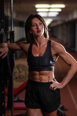 Fototapeta premium A strong woman athlete poses in the gym, demonstrating the devotion of fitness and muscle physique during training