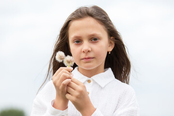 Young girl holding flower buds in a serene outdoor setting on a cloudy day