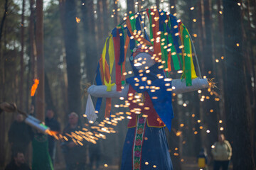 Celebration of a traditional festival with a colorful effigy surrounded by sparklers in a forest setting during daytime