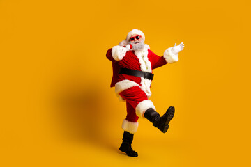 Funny dancing Santa Claus in red costume with sunglass having fun against yellow background, celebrating Christmas spirit