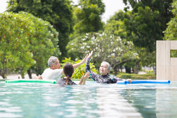 Senior Couple High-Fiving in Pool During Water Aerobics or Hydrotherapy, Aqua Fitness Class, Instructor and Older Adults Exercising with Pool Noodles