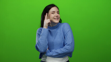 Woman in blue sweater gestures idea against vivid green background with thoughtful expression and...