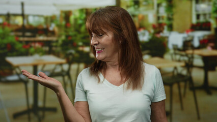 Hispanic senior woman smiling and gesturing with one hand extended in a cozy indoor restaurant...