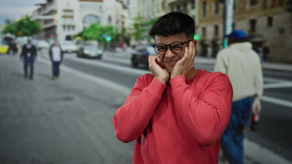 Young man in glasses expressing emotion on a bustling city street background with taxis and pedestrians passing by on a bright day.