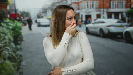 Fototapeta premium Woman gesturing and covering face while standing on busy street in outdoor urban setting against a backdrop of cars and buildings