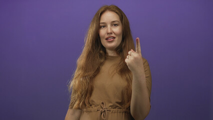 Young woman smiling and holding up two fingers in purple studio gesturing peace and victory; celebration.