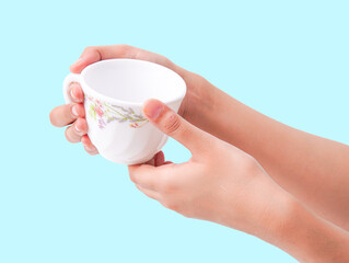 Two hands gently hold a floral patterned teacup against a serene blue