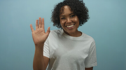 Smiling young african american woman waving hand in studio wearing a casual t shirt; friendly...