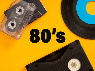 Audio Cassette, Vinyl Record and VHS Representing the 80's on Yellow Background
