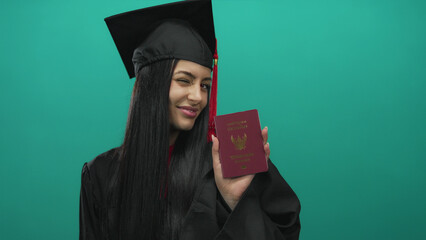 Graduated young woman in cap and gown holding thailand passport against green background,...