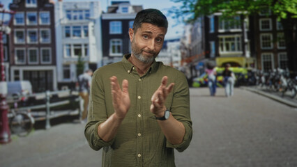 Man clapping hands on street by canal houses wearing green shirt with rolled sleeves and...
