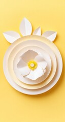 A delicate, layered paper flower design rests in a circle of pastel shades against a vibrant yellow background.