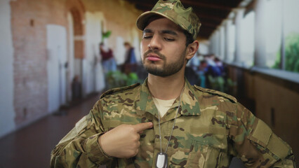 Young hispanic soldier in camouflage uniform with finger pointing to dogtag on sunlit restaurant...