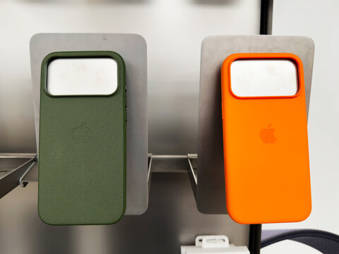 Two vibrant Ihone 17 Pro cases sit on a metal display panel, green and orange, with Apple branding