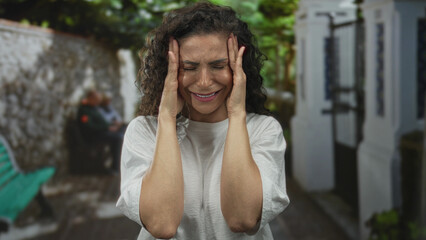 Young hispanic woman with closed eyes and furrowed brow holds temples for headache on sunlit...