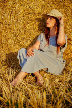 red-haired beautiful woman with hat in field with haystacks against blue sky