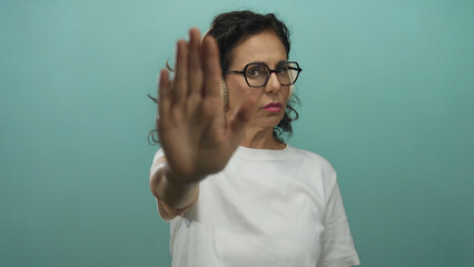 Woman gesturing stop with hand wearing headphones and glasses against isolated blue wall middle...