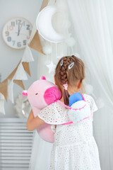 Young girl in white dress holding teddy bear and cloud backpack.