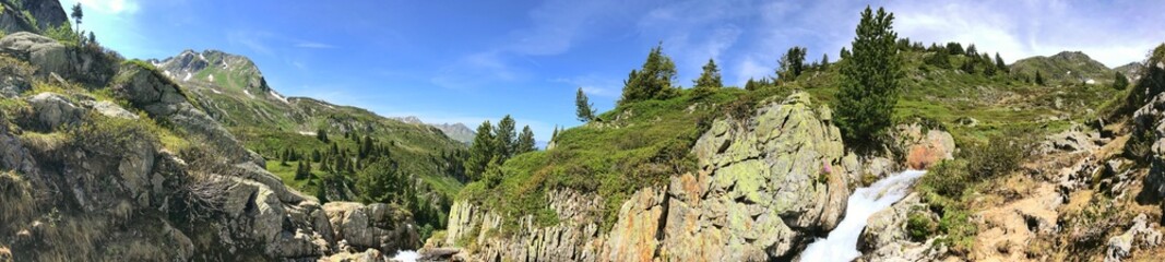 Panoramic view of a mountain landscape with trees and a flowing stream