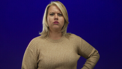 Woman pointing finger in studio setting wearing beige sweater with intense gaze and furrowed brow; disapproval.
