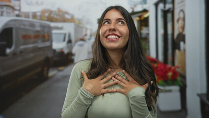 Young hispanic woman outdoors on street smiling with joy, surrounded by urban vehicles and vibrant flower shops, exuding happiness and contentment in a lively city scene.