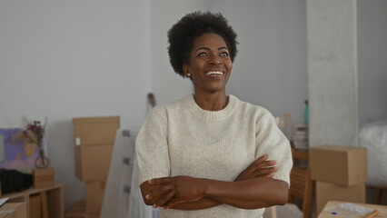 Woman stands confidently with crossed arms in a new home living room surrounded by moving boxes and...